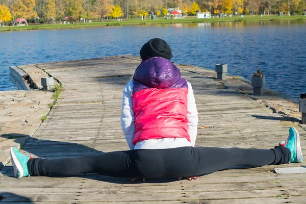 A beautiful girl with a slim figure in the black leggings and bright pink jacket is playing sports  in the autumn park in sunny weather. — Stock Photo, Image