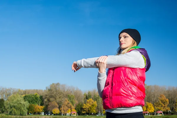 Güzel bir kız bir ince rakam siyah tayt ve parlak pembe ceket ile güneşli havalarda sonbahar parkta spor oynuyor.