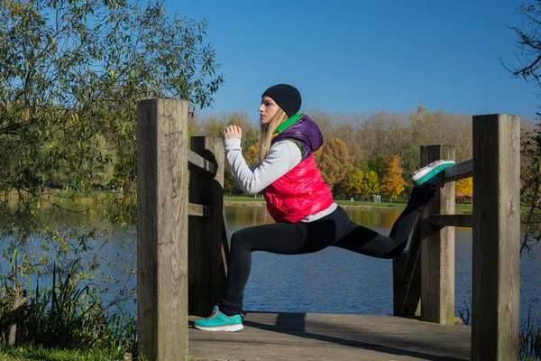 Güzel bir kız bir ince rakam siyah tayt ve parlak pembe ceket ile güneşli havalarda sonbahar parkta spor oynuyor.