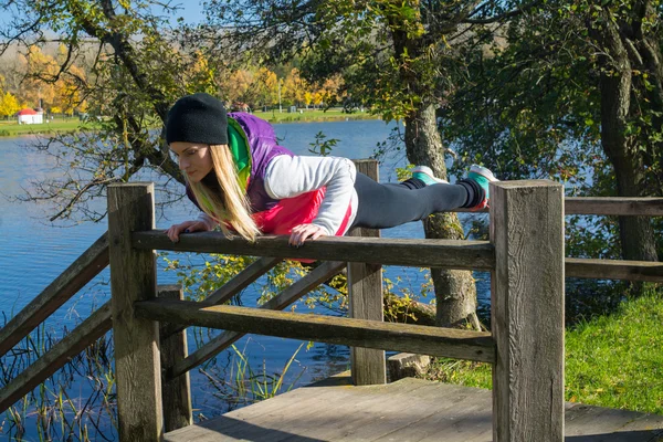 Güzel bir kız bir ince rakam siyah tayt ve parlak pembe ceket ile güneşli havalarda sonbahar parkta spor oynuyor.