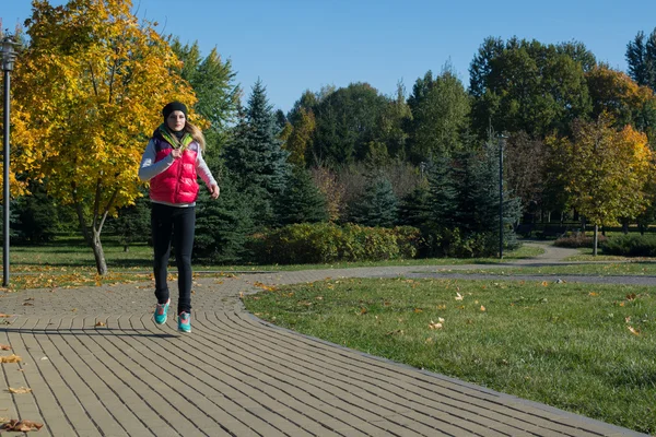 Güzel bir kız bir ince rakam siyah tayt ve parlak pembe ceket ile güneşli havalarda sonbahar parkta spor oynuyor.