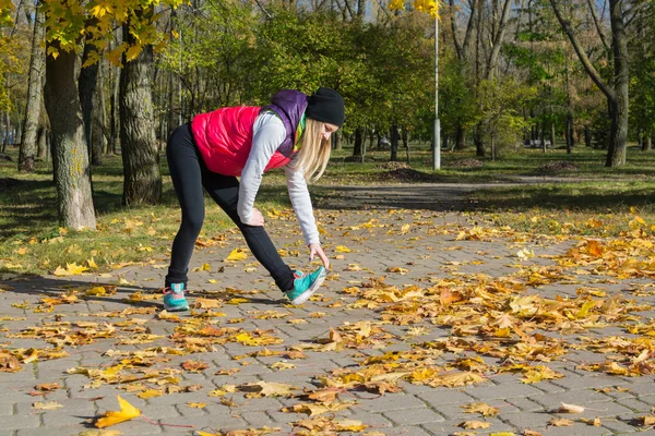 Güzel bir kız bir ince rakam siyah tayt ve parlak pembe ceket ile güneşli havalarda sonbahar parkta spor oynuyor.