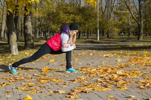 Güzel bir kız bir ince rakam siyah tayt ve parlak pembe ceket ile güneşli havalarda sonbahar parkta spor oynuyor.