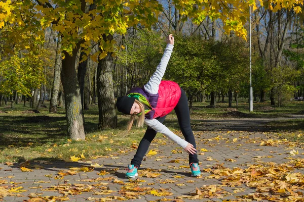 Güzel bir kız bir ince rakam siyah tayt ve parlak pembe ceket ile güneşli havalarda sonbahar parkta spor oynuyor.