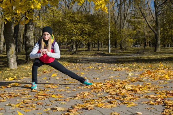 Güzel bir kız bir ince rakam siyah tayt ve parlak pembe ceket ile güneşli havalarda sonbahar parkta spor oynuyor.