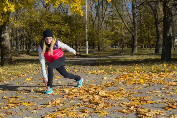 Güzel bir kız bir ince rakam siyah tayt ve parlak pembe ceket ile güneşli havalarda sonbahar parkta spor oynuyor.