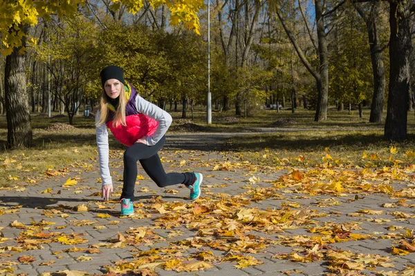 Güzel bir kız bir ince rakam siyah tayt ve parlak pembe ceket ile güneşli havalarda sonbahar parkta spor oynuyor.