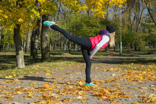 A beautiful girl with a slim figure in the black leggings and bright pink jacket is playing sports  in the autumn park in sunny weather. — Φωτογραφία Αρχείου