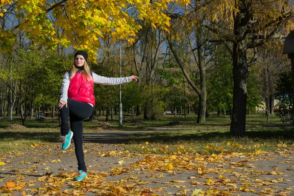 Güzel bir kız bir ince rakam siyah tayt ve parlak pembe ceket ile güneşli havalarda sonbahar parkta spor oynuyor.