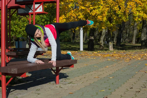 Güzel bir kız bir ince rakam siyah tayt ve parlak pembe ceket ile güneşli havalarda sonbahar parkta spor oynuyor.