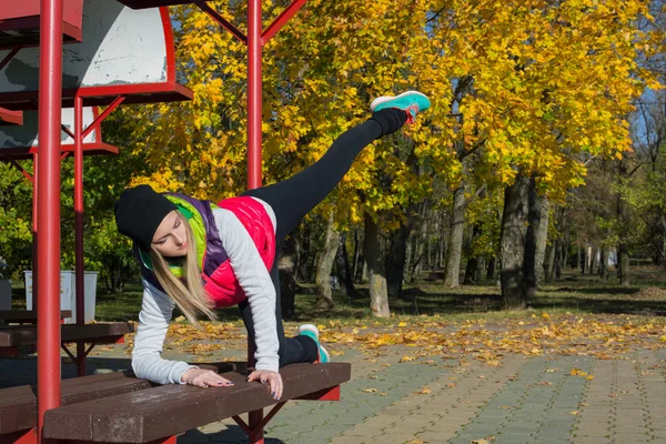 Güzel bir kız bir ince rakam siyah tayt ve parlak pembe ceket ile güneşli havalarda sonbahar parkta spor oynuyor.