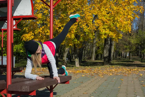 Güzel bir kız bir ince rakam siyah tayt ve parlak pembe ceket ile güneşli havalarda sonbahar parkta spor oynuyor.