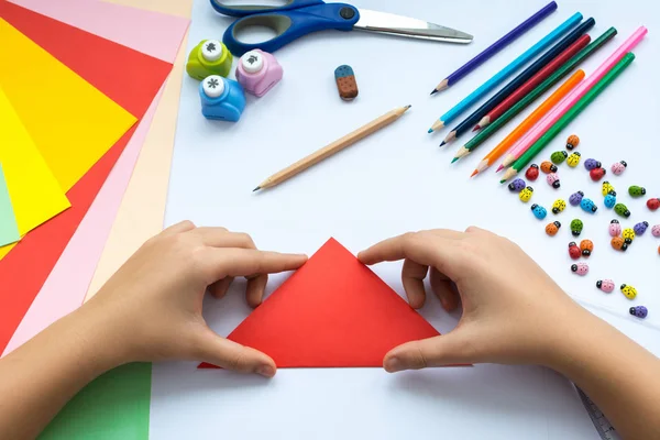 Children's hands do origami  bird from red paper.