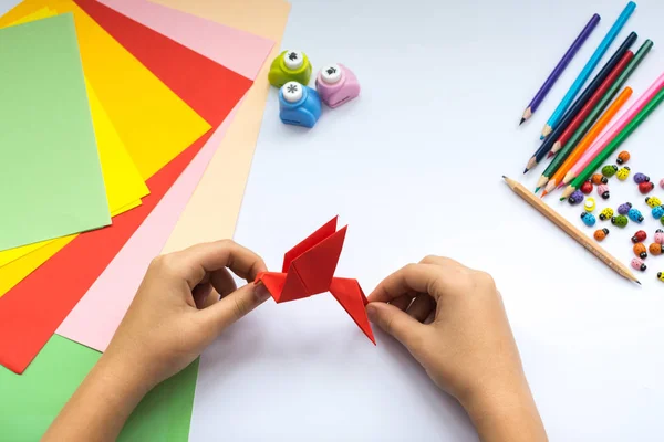 Children's hands do origami  bird from red paper.