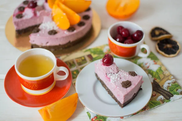 RAW cake, red cup of camomile tea, cherry in a cup, a persimmon on a wooden background