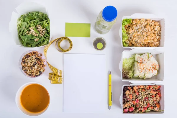 Un plan nutritionnel sain. Livraison de repas frais quotidiens. Nourriture de restaurant pour un, légumes, viande et fruits dans des boîtes en papier d'aluminium, charbon de désintoxication, carte de visite, carnet et crayon sur fond de bois blanc . — Photo