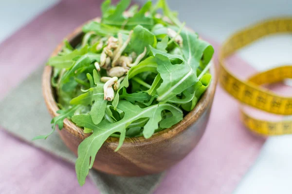 Salada de rúcula com brotos de sementes em uma tigela de madeira e uma fita métrica. close-up com um foco suave — Fotografia de Stock