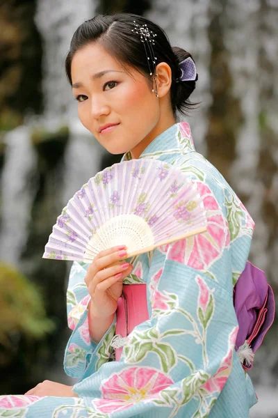 Young Asian girl in a traditional kimono with a fan in a natural and picturesque outdoor environment