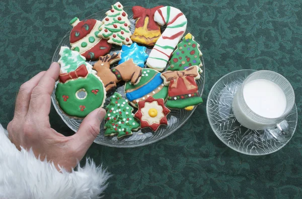 Santa Claus agarrando uno de los muchos colores decorados y esmerilados cortar galletas de Navidad — Foto de Stock