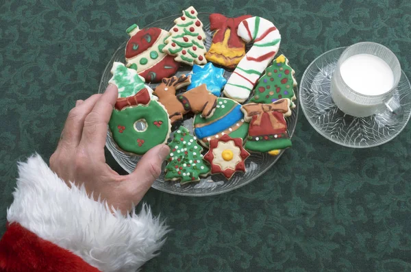 Santa Claus agarrando uno de los muchos colores decorados y esmerilados cortar galletas de Navidad — Foto de Stock