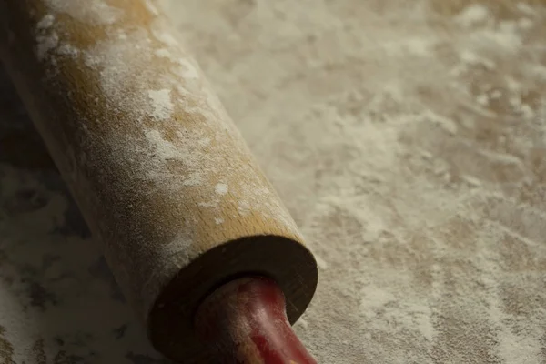 A closeup of a wooden flowered rolling pin on a blurred wooden surface 