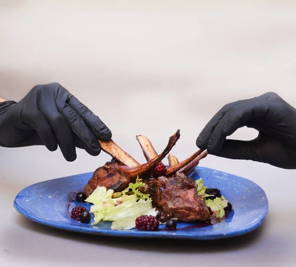A man in black gloves tears apart pork ribs with his hands