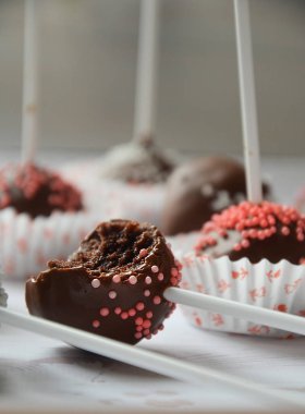 Çikolatada beyaz bir çubuğun üzerine kırmızı toplar serpiştirilmiş kek.