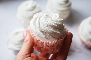 Öndeki kırmızı sepetin içine krema serpilmiş beyaz marşmelovlar.