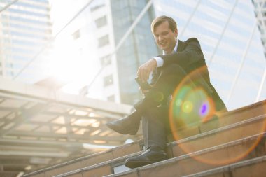 Takım elbiseli iş adamı akşam saatlerinde akıllı telefon kullanarak rahatlar, güneş ışığı ve iş konseptiyle.