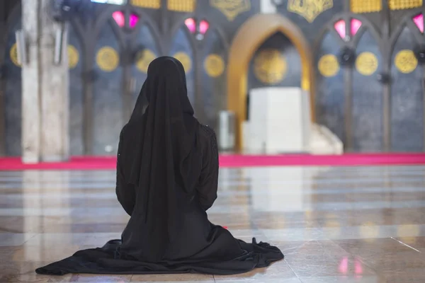 Ung muslimsk kvinna i svart klänning sitter ensam i moskén, Bakifrån. — Stockfoto