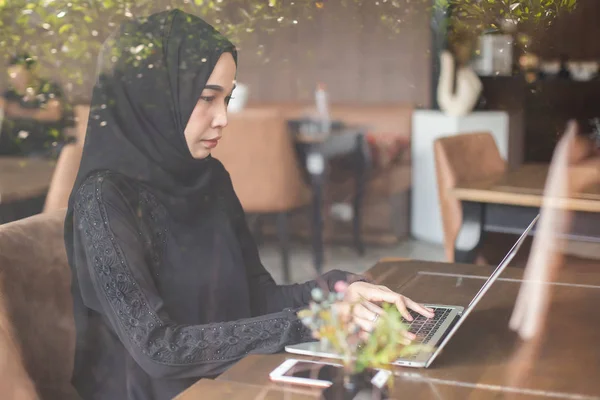 亚洲的穆斯林妇女，头戴黑色头巾，每天早上在咖啡店里与笔记本电脑一起工作. — 图库照片