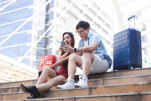 Junges Paar Mann und Frau mit Gepäck suchen Smartphone Lächeln und glücklich in Business-Stadt, Paar Reisekonzept. — Stockfoto