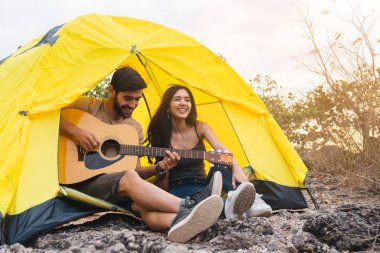 Dağda çadır kurmuş, akşam gitarlı romantik bir çift. Kamp gezisi konsepti..