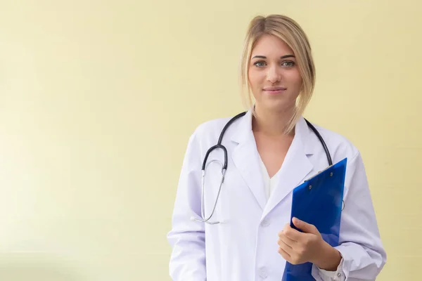 Retrato hermosa mujer médico de pie celebración carpeta con estetoscopio cerca de fondo amarillo en el hospital . — Foto de Stock