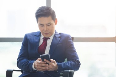 Asyalı işadamı internette akıllı telefon kullanarak ofiste çalışıyor..