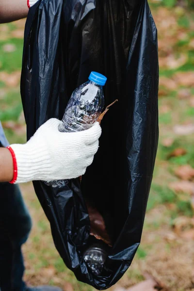 Close up mão jovem voluntários homem manter garrafa de plástico colocar em sacos de lixo área de limpeza no parque, Reduzir o plástico, reduzir o aquecimento global . — Fotografia de Stock