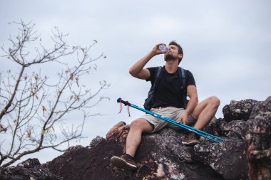 Sırt çantalı adam oturmuş, içme suyu içiyor dağda eğleniyor..