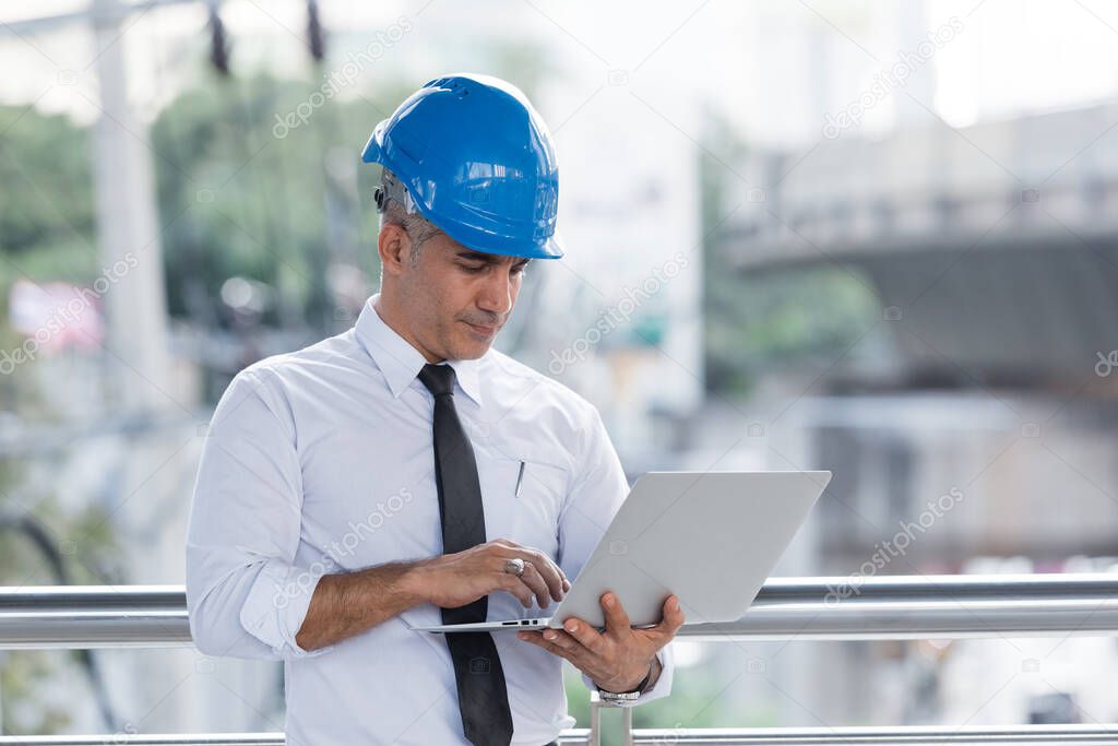 Engineering man wear blue helmet working with laptop outdoor building office.