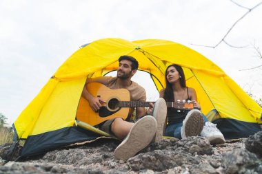 Dağda çadır kurmuş, akşam gitarlı romantik bir çift. Kamp gezisi konsepti..