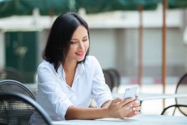 Kafede akıllı telefon kullanan genç bir kadın.