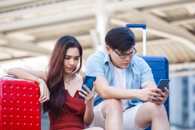 Bagajı olan Asyalı çift, konaklama ve turistik mekan için akıllı telefon kullanıyor..