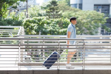 Bagajı olan Asyalı yakışıklı adam tatil zamanı yürüyor, seyahat konsepti..