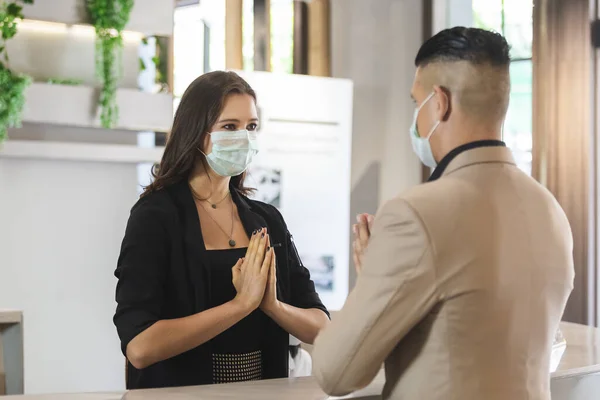 woman hotel receptionist wearing medical mask and visitor greeting Wai (Thai Greetings ) is a form of thai culture instead of handshake for prevent infection coronavirus covid 19