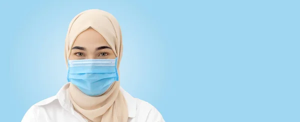 青い背景に感染ウイルスを防ぐために医療マスクをした顔のイスラム教徒の女性を閉じて — ストック写真