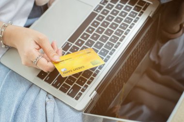 Bilgisayarda, ödeme ve online alışveriş için kredi kartı tutan kadının elini kapat..