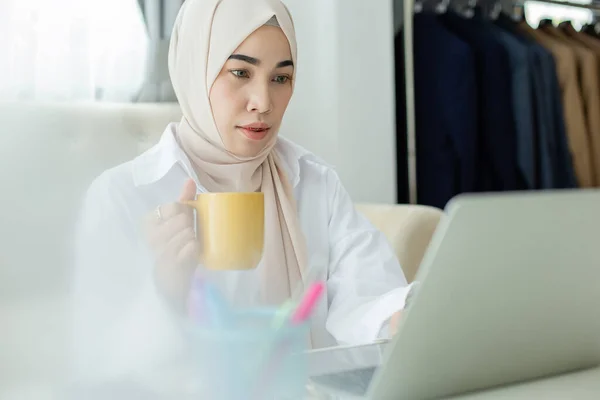 亚洲漂亮的穆斯林妇女 带着笔记本电脑在家拿着咖啡杯 从家里的观念出发工作 — 图库照片