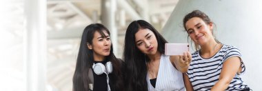 Bir grup güzel kadın şehirde otururken akıllı telefondan eğleniyor ve selfie çekiyor..