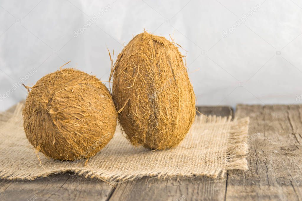Coconut nuts, mature, on a rustic jute base on a wooden table with a white background