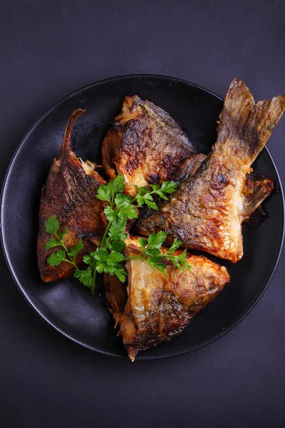 Pescado frito en un plato negro decorado con perejil fresco —  Fotos de Stock