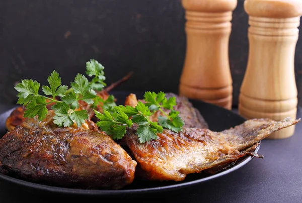 Pescado frito en un plato negro decorado con perejil fresco — Foto de Stock